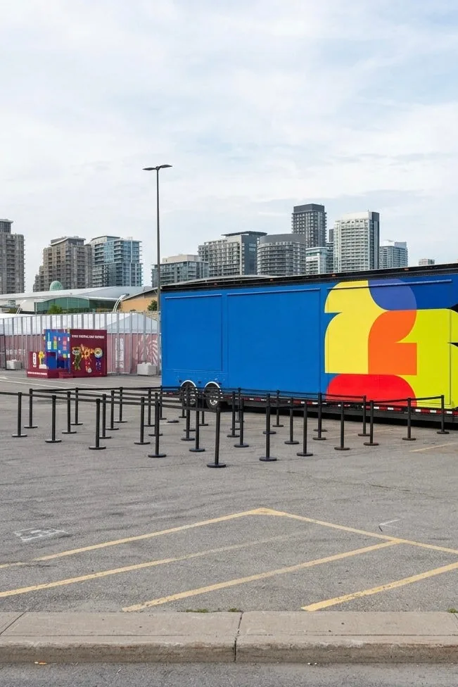Black belt stanchions set out across a parking lot beside a brightly wrapped event trailer