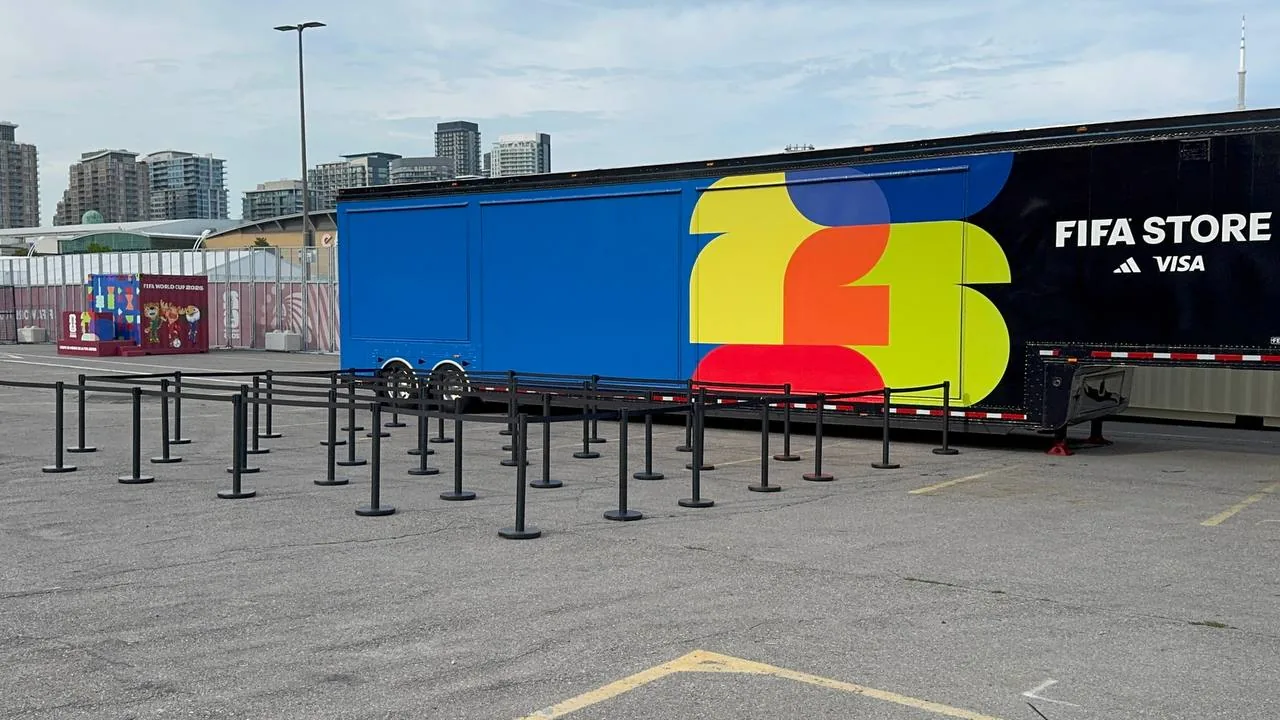 A long run of black belt posts set out across asphalt beside a branded event trailer