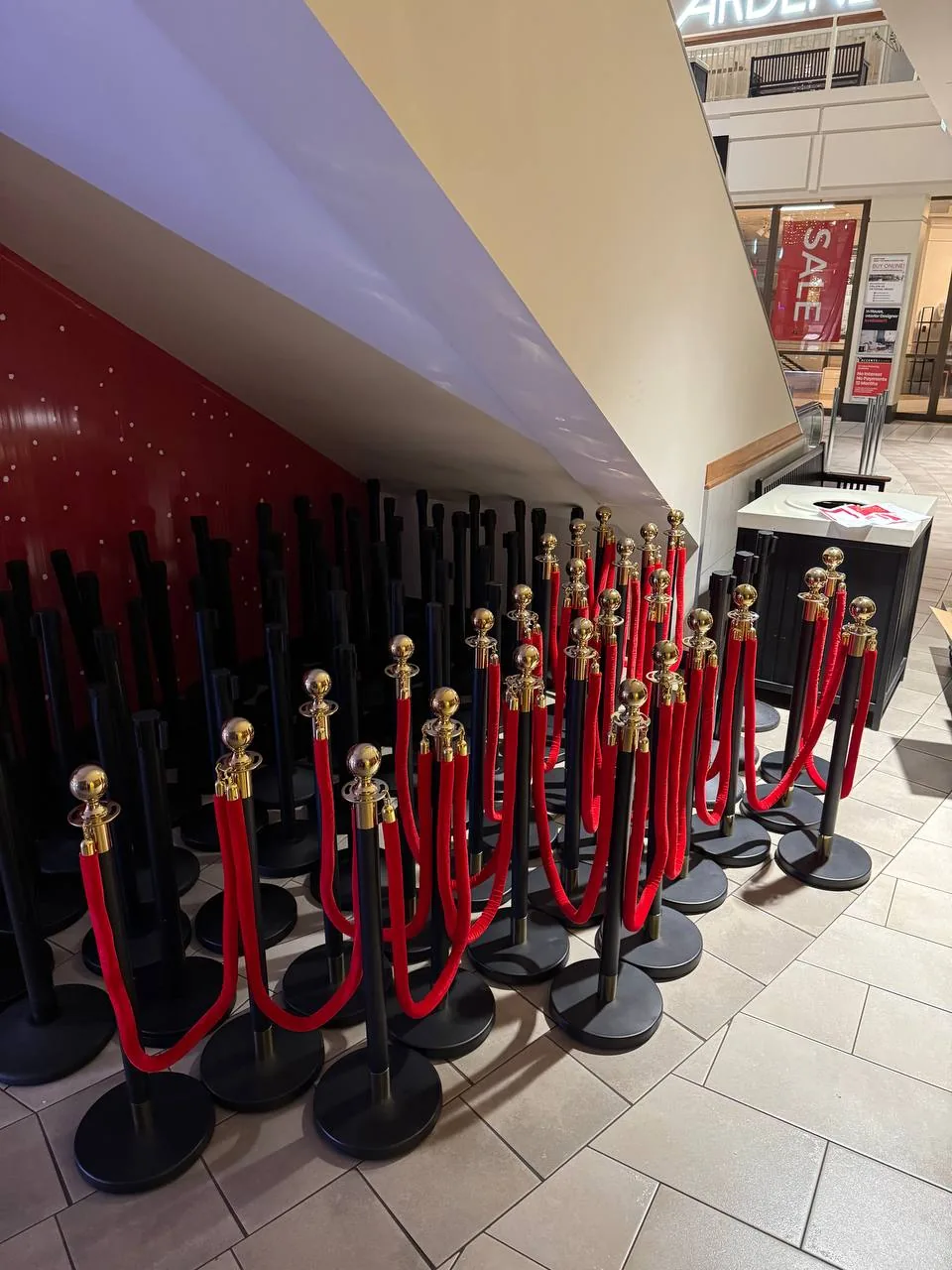 Rows of black posts with red ropes staged along a mall concourse before an event