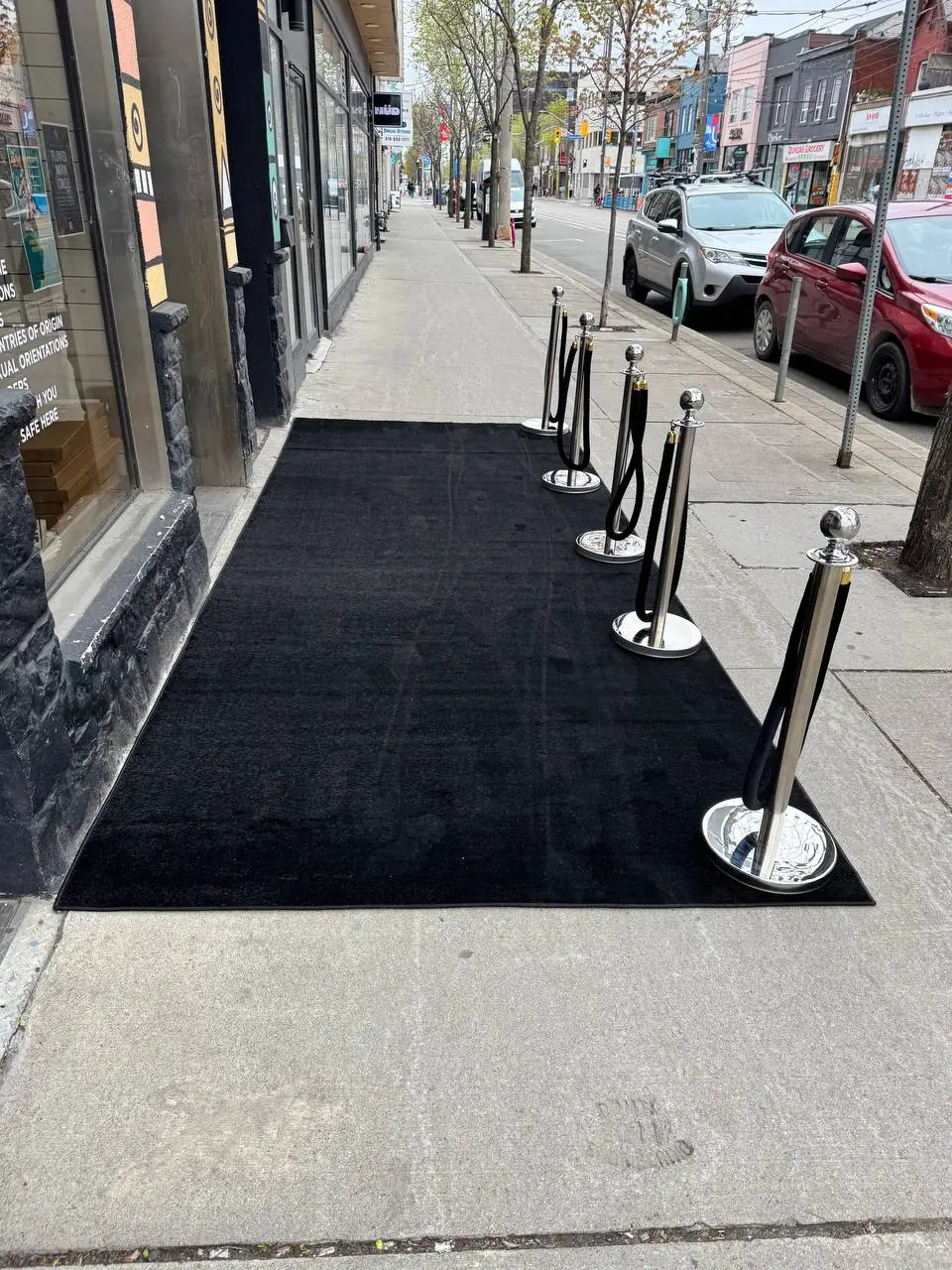 Silver posts holding the edge of a black carpet runner laid along a shopfront pavement