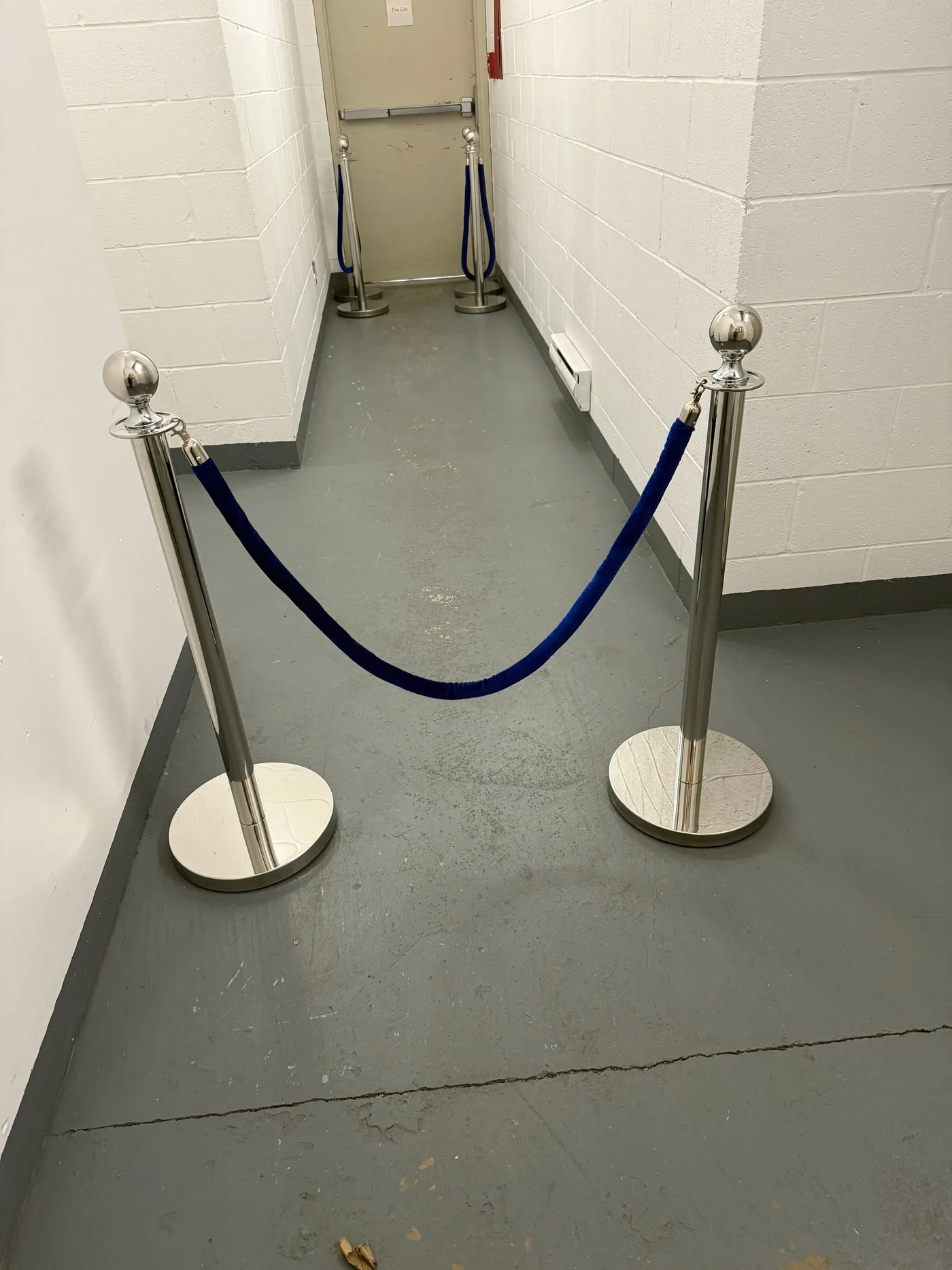 A deep blue velvet rope strung between silver posts in a plain service corridor